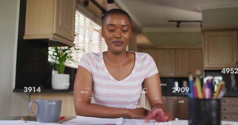 Young woman organizing bills and paperwork at home kitchen table with focused expression