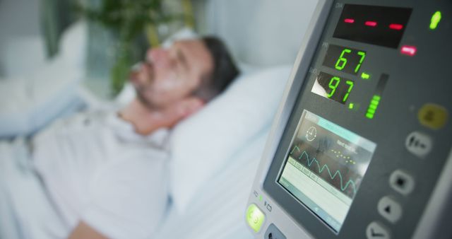 View of a male patient lying in a hospital bed with vital signs being monitored on a screen. Ideal for illustrating themes such as healthcare, patient care, medical technology, and critical care situations.