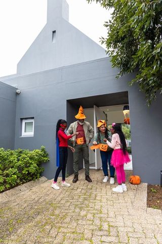 African american family celebrating halloween on modern porch with pumpkin buckets