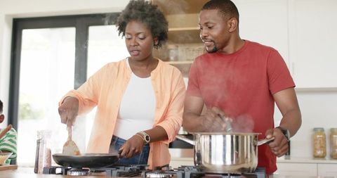 African american couple cooking together in bright kitchen, flipping pan and stirring pot
