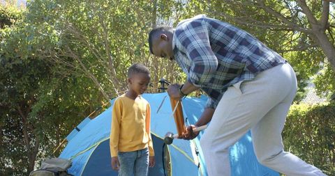 African american father assembling blue tent with son backyard camping bonding using mallet
