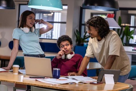 Diverse college students collaborating with laptop and headsets in modern study space