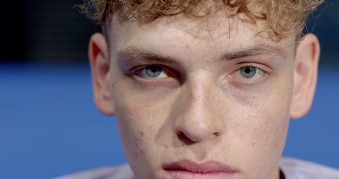 Portrait of freckled man with curly hair on blurred blue background
