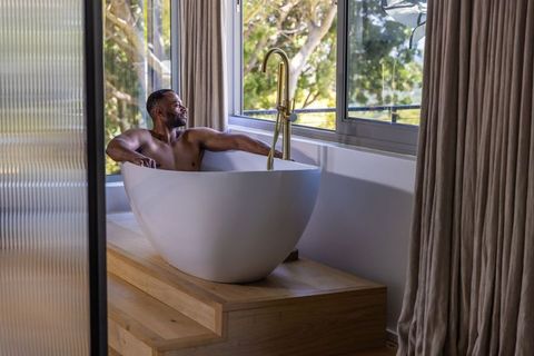 Mature african american man relaxing in freestanding bathtub by window with greenery view