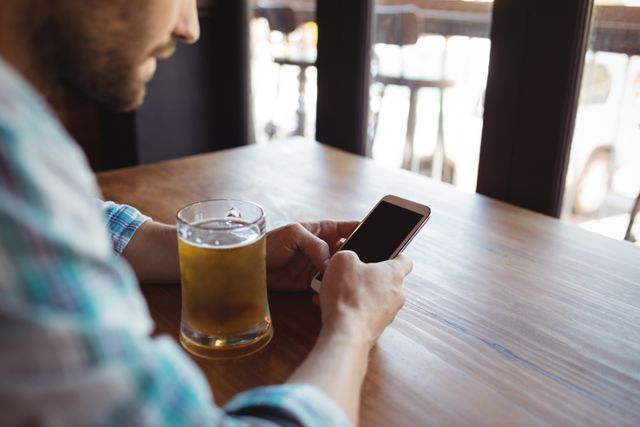 Man using mobile phone while having beer in bar