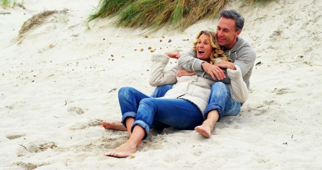 A relaxed couple sits and embraces on a sandy beach. The scene conveys joy, love, and togetherness. Suitable for use in vacation promotions, lifestyle blogs, romantic getaway advertisements or content about happiness.