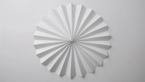White paper rosette radiating geometric pleats and soft shadows on neutral gray background