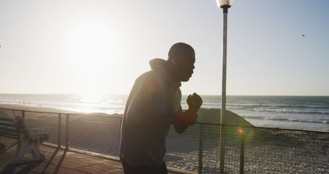 Boxer training by the seaside at sunrise with earphones in, creating a focused and athletic atmosphere. Ideal for conveying themes of dedication, morning routines, fitness, and motivation, perfect for use in blogs, fitness advertising, motivational posters, and campaigns promoting an active lifestyle along the beach.