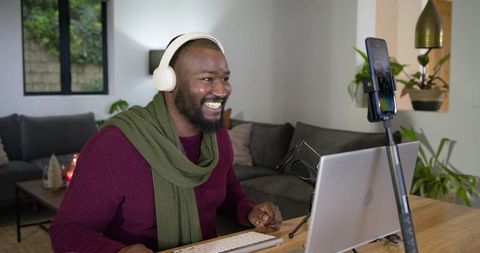 Smiling african american man wearing headphones recording remote meeting with laptop