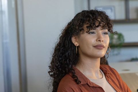 Confident african american woman in home office wearing terracotta shirt and gold hoops