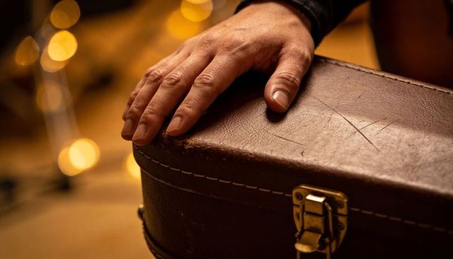 Resting right hand pressing worn leather case with brass latch and warm bokeh lights