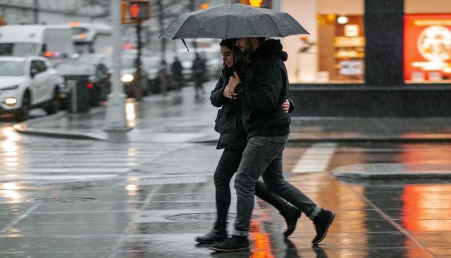 Couple sharing umbrella while crossing rainy urban crosswalk at night with reflections