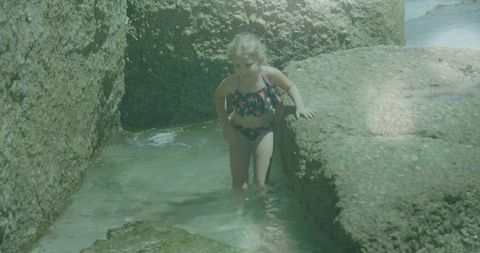 Curious girl exploring tide pools amidst rocky boulders
