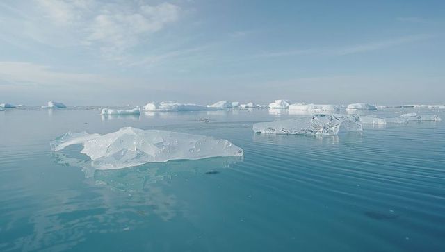 Floating translucent ice chunk creating ripples on turquoise arctic sea with tabular ice