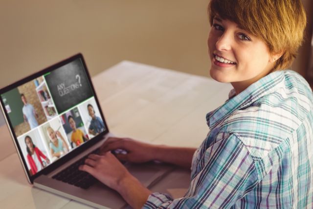 Young person smiling while attending virtual classroom and interacting with multiple people on laptop screen. Ideal for illustrating online education, remote learning, virtual communication, e-learning platforms, and modern technology in education.