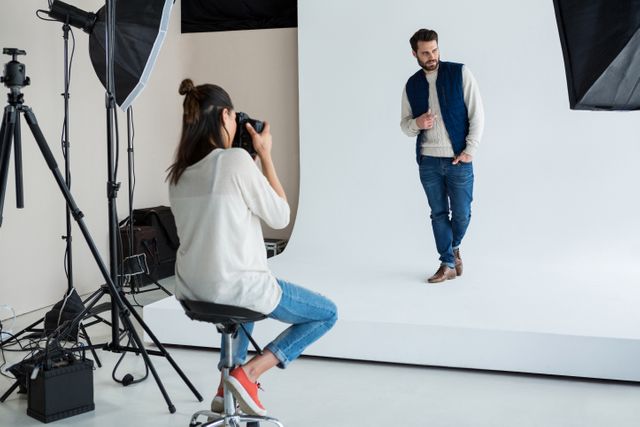 Male model posing for a photographer in a professional studio. The model is dressed in casual wear, including jeans and a jacket, while the photographer captures the shot using professional camera equipment and lighting. Ideal for use in fashion industry promotions, photography tutorials, model agency advertisements, and creative project showcases.