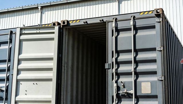 Opening shipping container doors revealing empty ribbed interior at industrial warehouse