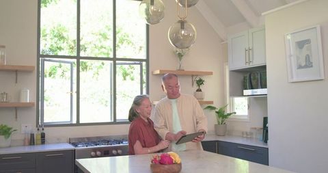 Senior asian couple using tablet in bright modern kitchen, technology lifestyle for seniors