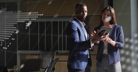 Two professionals collaborating over tablet in modern office boardroom with glass reflections