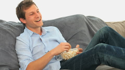 Happy Man Relaxing on Sofa Watching TV with Popcorn