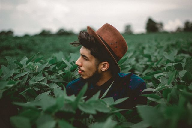 Young man wearing brown hat surrounded by green foliage - Download Free Stock Photos Pikwizard.com