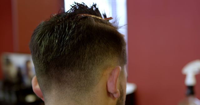 Close-up of a young biracial man getting a haircut at a barbershop. Precision and style are evident in the barber's work on the trendy hairstyle.