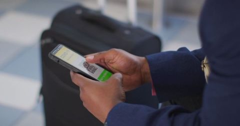 Traveler Holding Smartphone with COVID Passport Near Luggage