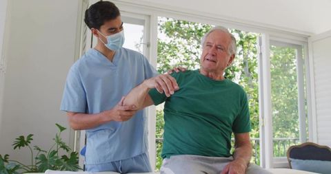 Home healthcare worker assisting senior man with arm therapy during daytime visit
