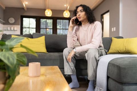 Non-binary person talking on phone while relaxing on gray sofa in cozy modern living room