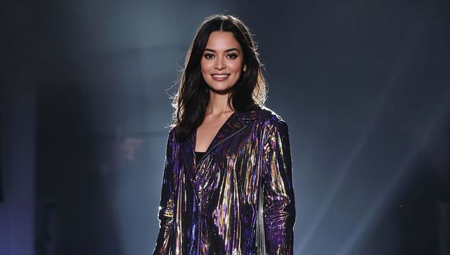 Smiling model posing on runway wearing iridescent metallic coat under spotlight