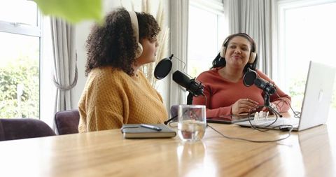 Two women recording podcast in home studio with microphones, laptop, headphones, notepad