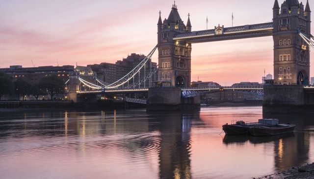 Sunset glow over tower bridge and river thames with moored barges and city reflections