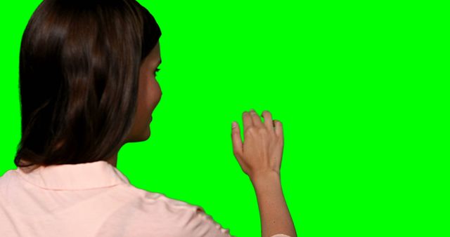 Woman pretending to touch digital screen against green screen