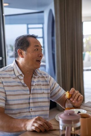 Asian Man Relaxing at Home with Pastry and French Press Coffee