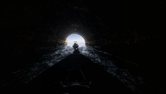Silhouetted motorboat exiting dark sea tunnel toward bright ocean horizon