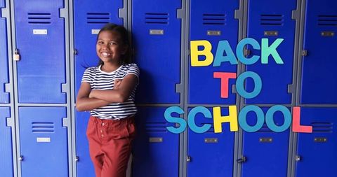 Confident student leaning on blue lockers with colorful back to school letters