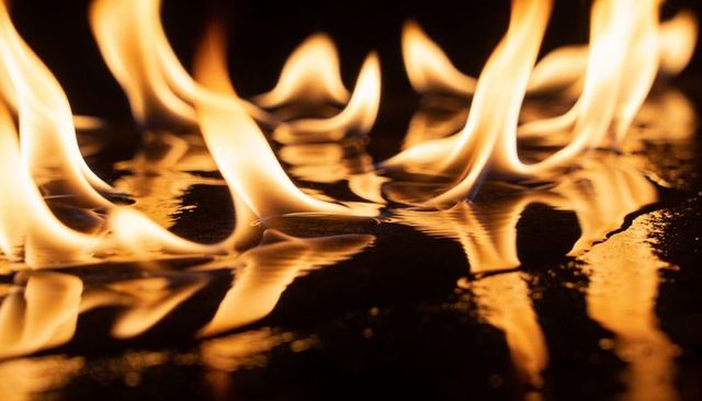 Dancing orange flames reflecting on wet surface with liquid ripples and warm glow