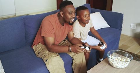 Father and Son Enjoying Video Game at Home with Popcorn