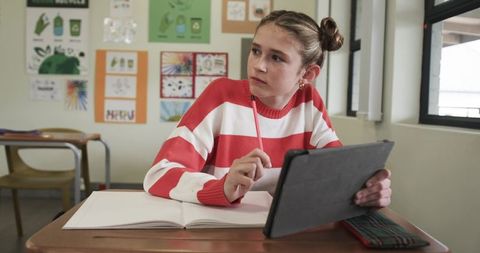 Young Female Student Using Tablet and Notebook in Classroom