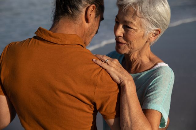 Senior Caucasian couple enjoying time at the beach on a sunny day, dancing on the beach, with sea in the background. Summer tropical beach vacation.