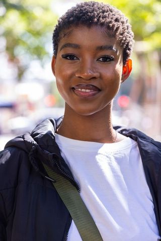 Smiling young african woman on sunny street wearing puffer jacket and white tee