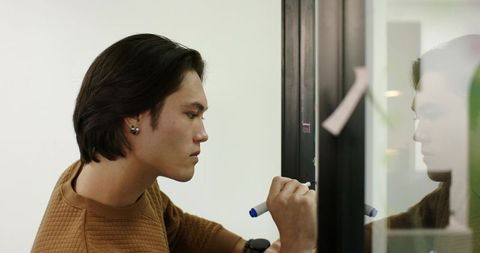 Young professional brainstorming on glass surface in modern office