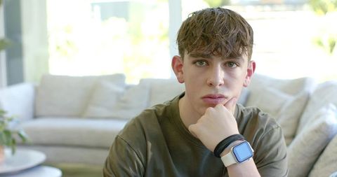 Teen male resting on sofa propping chin and gazing forward wearing smartwatch