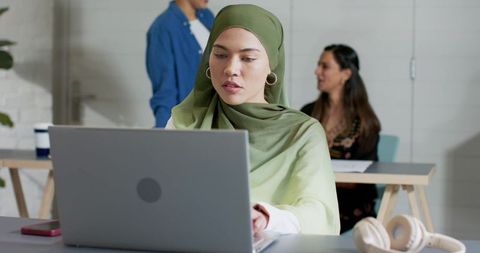 Young professional woman in olive hijab working on laptop in modern coworking space team