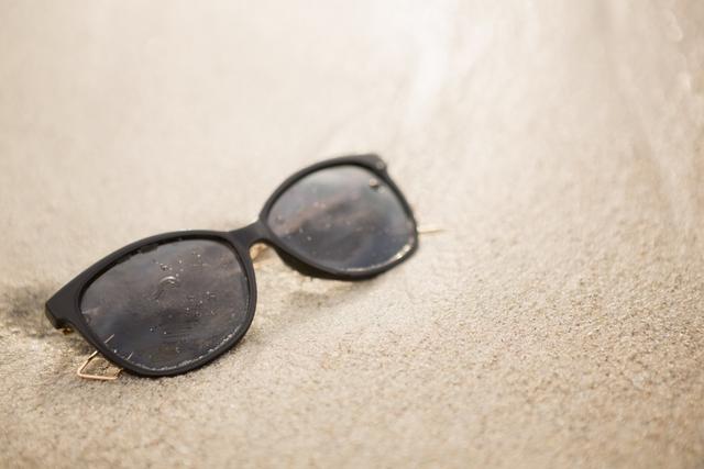 Sunglasses rest on sandy beach, capturing the essence of a relaxing summer vacation. Ideal for use in travel brochures, vacation advertisements, eyewear promotions, and beach-themed websites. Conveys a sense of leisure, sun protection, and outdoor enjoyment.
