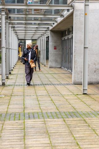 Diverse men walking under metal canopy in modern urban plaza with takeaway and smartphone