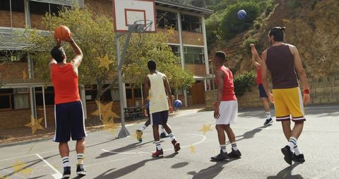 Five male players shooting and passing on outdoor school basketball court during practice