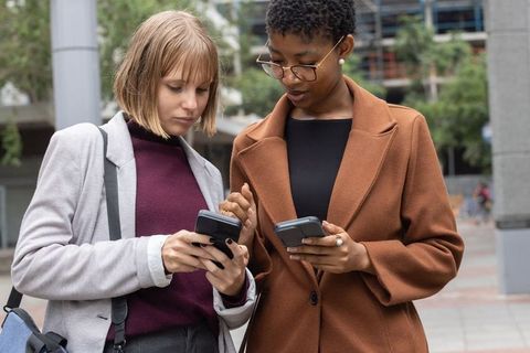 Diverse professional women comparing smartphones and sharing information in urban plaza