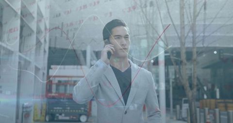 Young asian executive talking on phone with financial data graph overlay in urban plaza