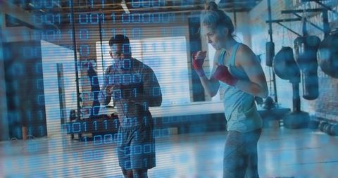 Female boxer training with coach in industrial gym showing digital binary overlay